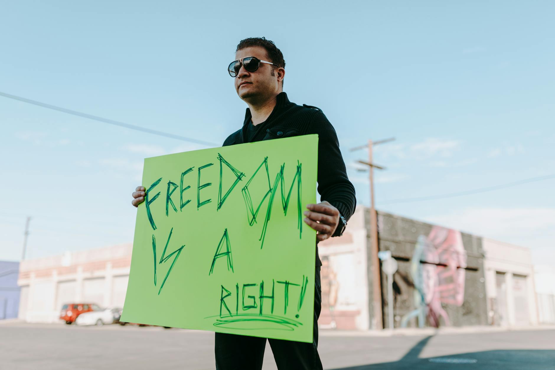 a man in black long sleeves holding green placard with message